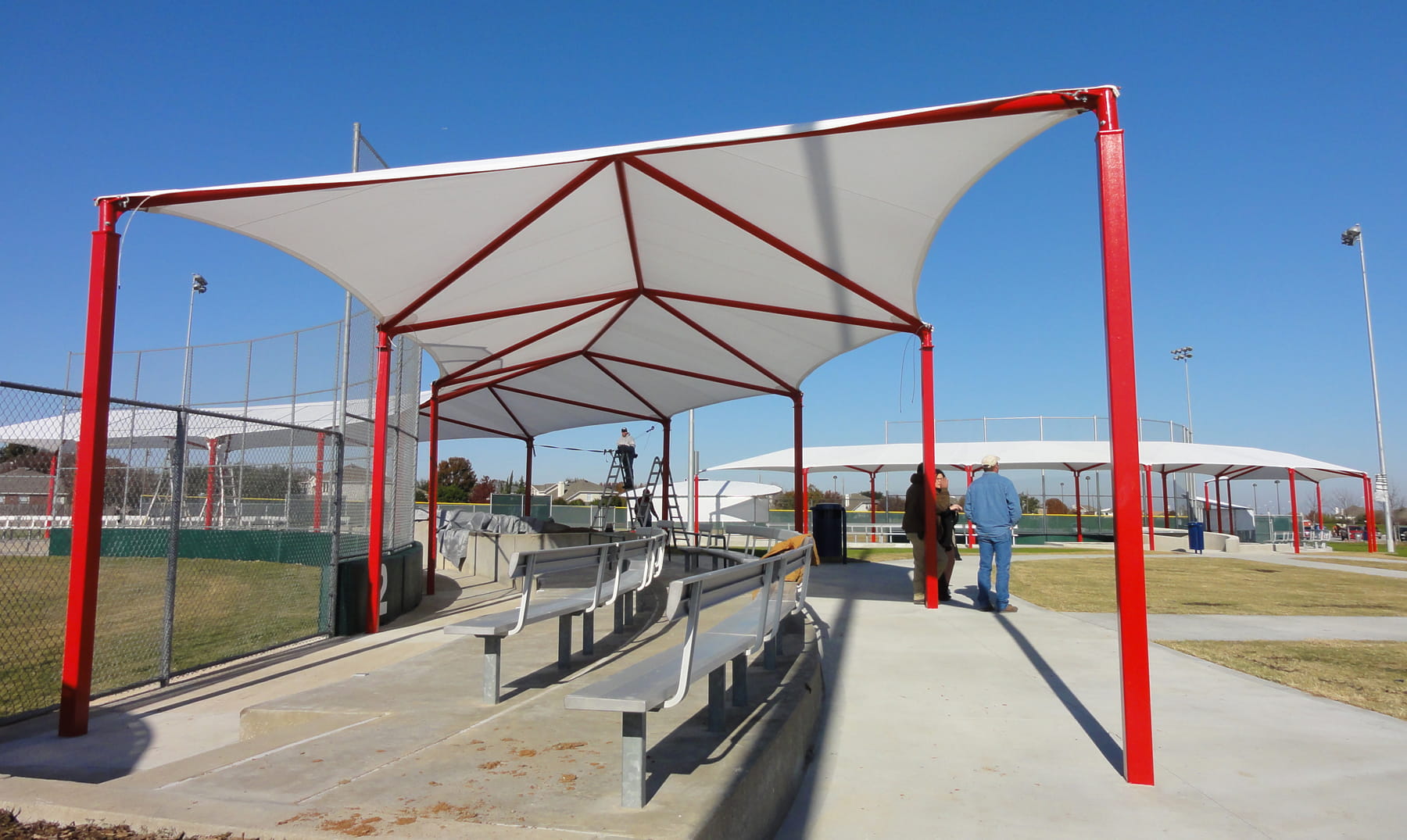 Red and white USA Shade Wrap-around Hip structure with benches underneath, set against a clear blue sky.