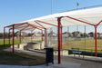 USA Shade Wrap-around Hip covering seating area at a sports field with red frames and white roof, surrounded by a fence and grass.