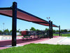 Outdoor sports facility with a USA Shade Slanted Cantilever Framed covered area, benches, and sports equipment under a clear blue sky.