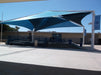 Large blue USA Shade Mariner Pyramid Shade over a concrete area with a school building in the background