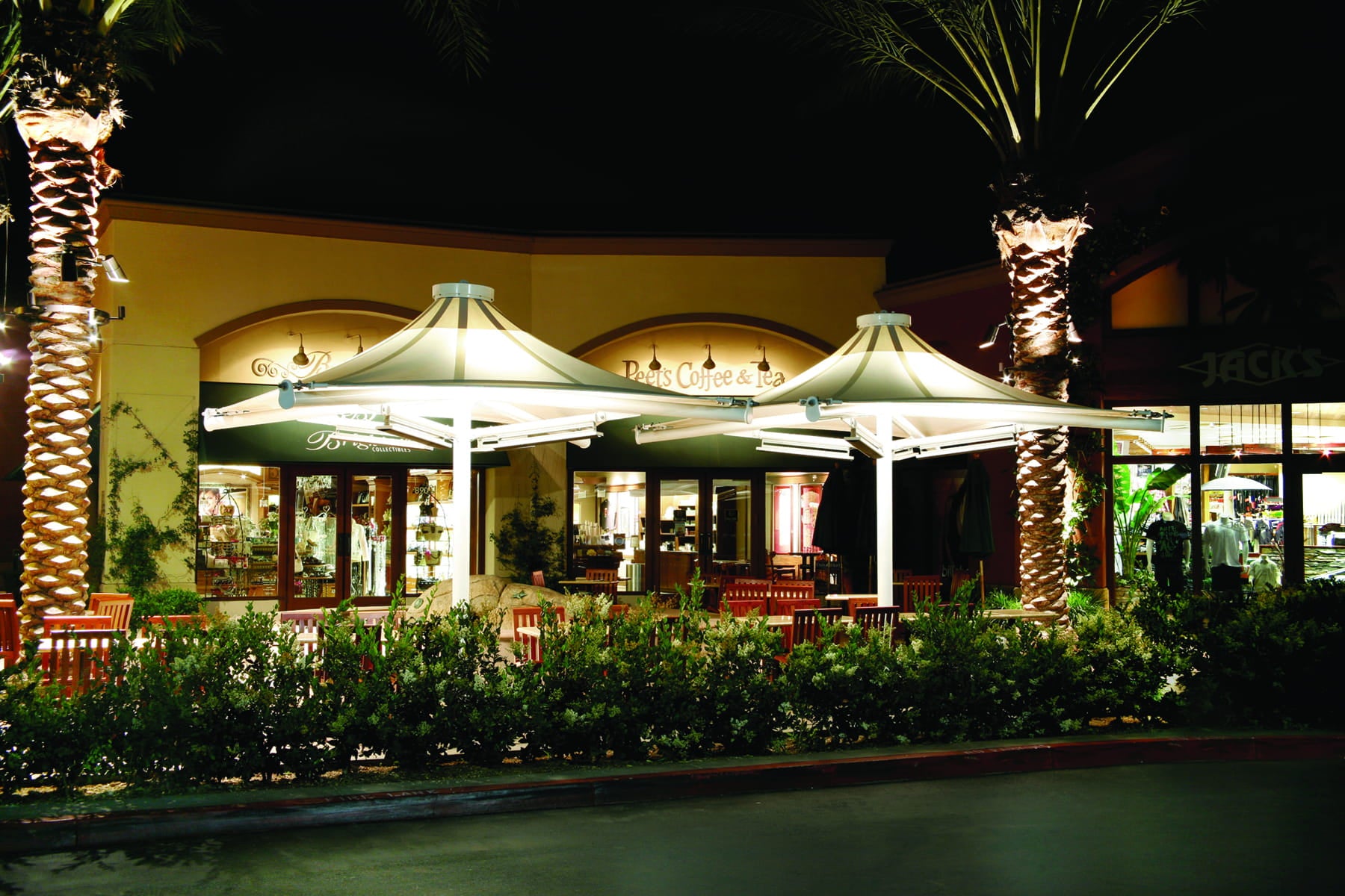 Outdoor restaurant patio with USA Shade 4-point Twilite Umbrellas and palm trees at night