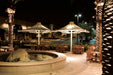 Outdoor dining area with tables, chairs, and USA Shade 4-point Twilite Umbrellas at night.