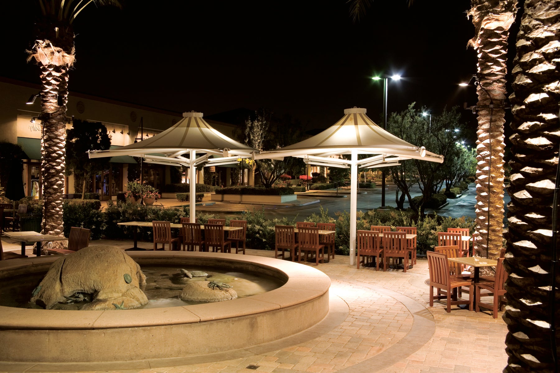 Outdoor dining area with tables, chairs, and USA Shade 4-point Twilite Umbrellas at night.