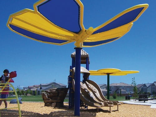 Children's playground with a large USA Shade Butterfly Wings Shade against a clear blue sky.