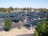 Parking lot with cars under green USA Shade Full Hip Cantilever Shades and a building in the background
