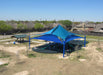 Blue USA Shade Multi-layer Super Span Pyramid Shade structure in a park with trees and buildings in the background