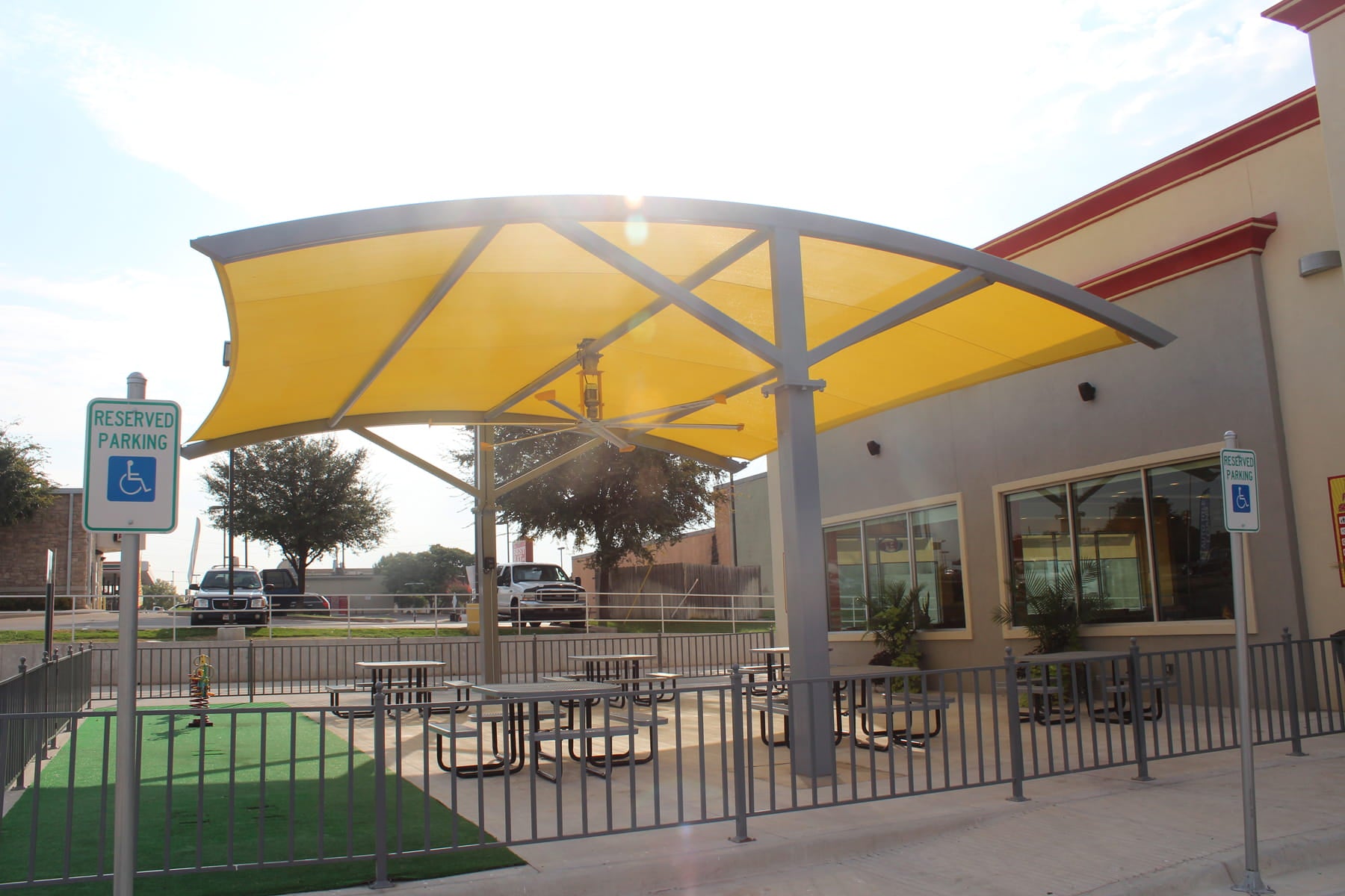 Yellow USA Shade Panorama Cantilever over outdoor seating area with tables and chairs, building in the background