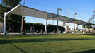 Outdoor event with people under a large white USA Shade Full Hip Cantilever Shade on a grassy field.
