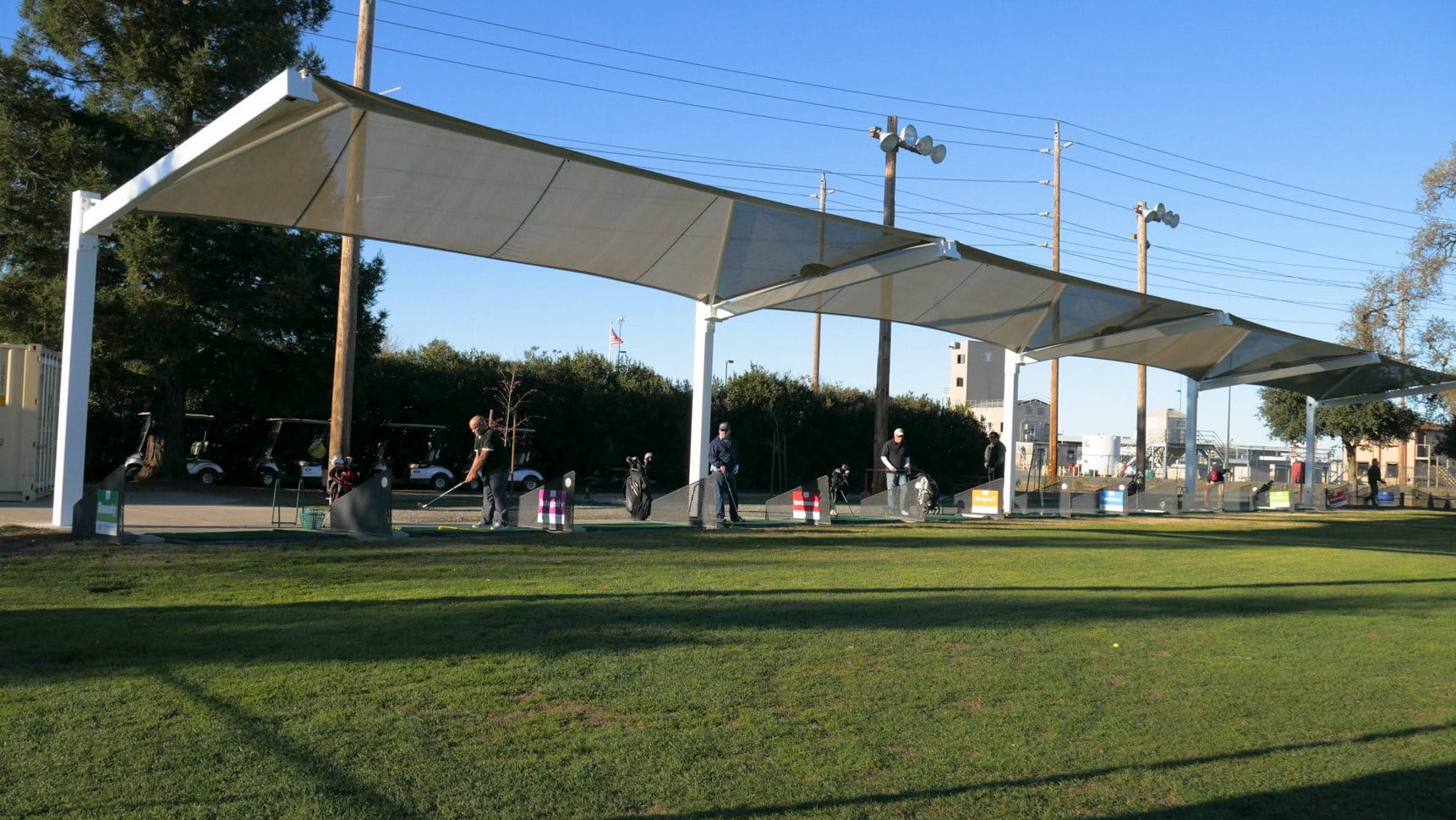 Outdoor event with people under a large white USA Shade Full Hip Cantilever Shade on a grassy field.