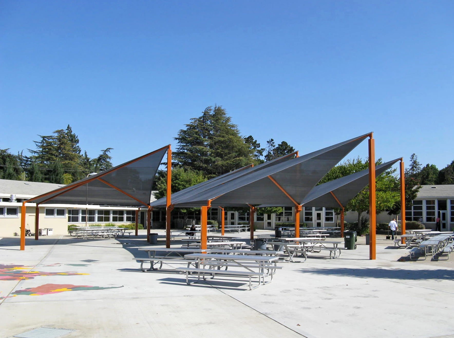 Outdoor seating area with USA Shade Wave Shade and picnic tables in a school setting