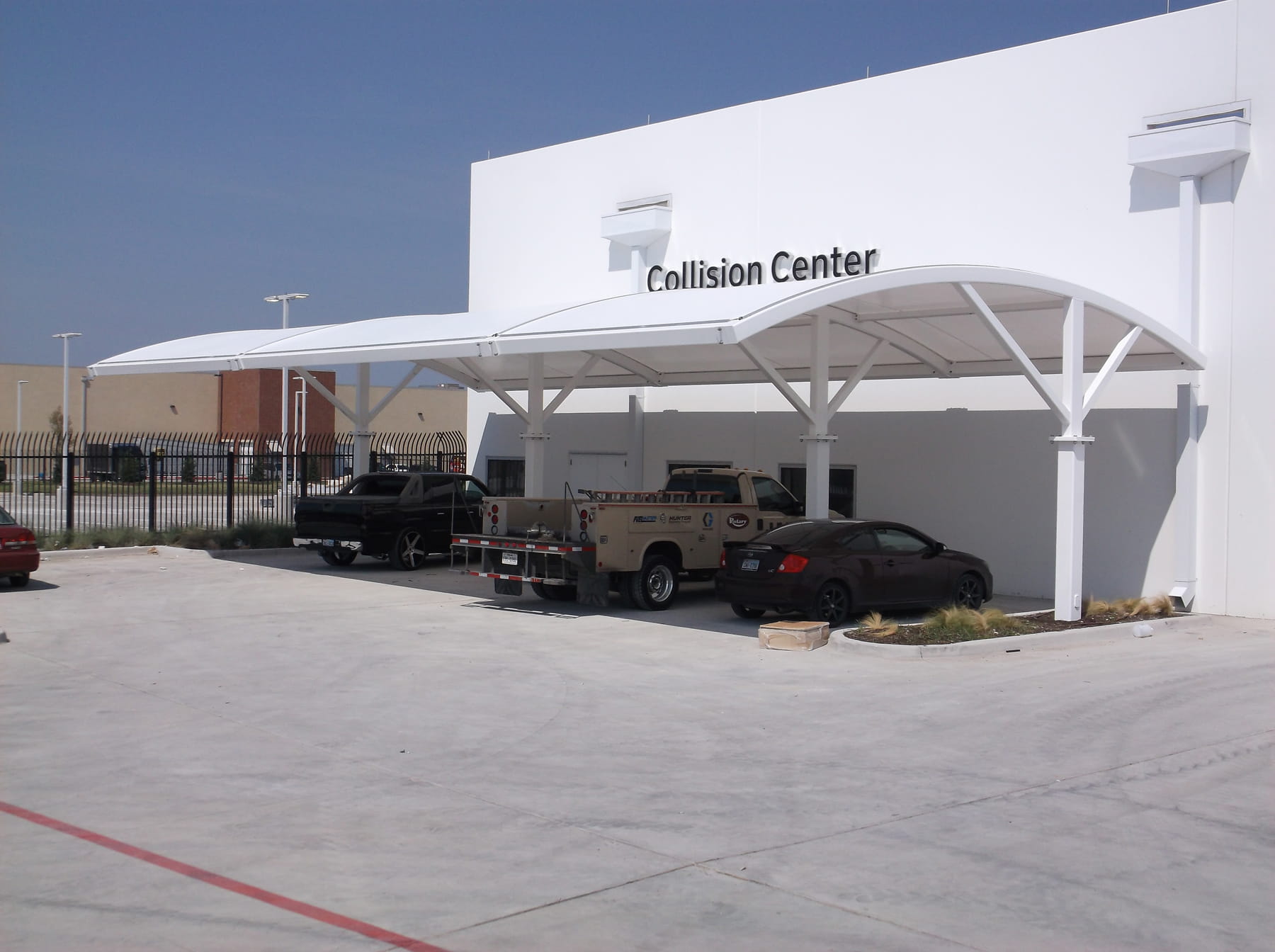 White building with 'Collision Center' sign, cars parked in front with USA Shade Panorama Cantilever providing shade for cars