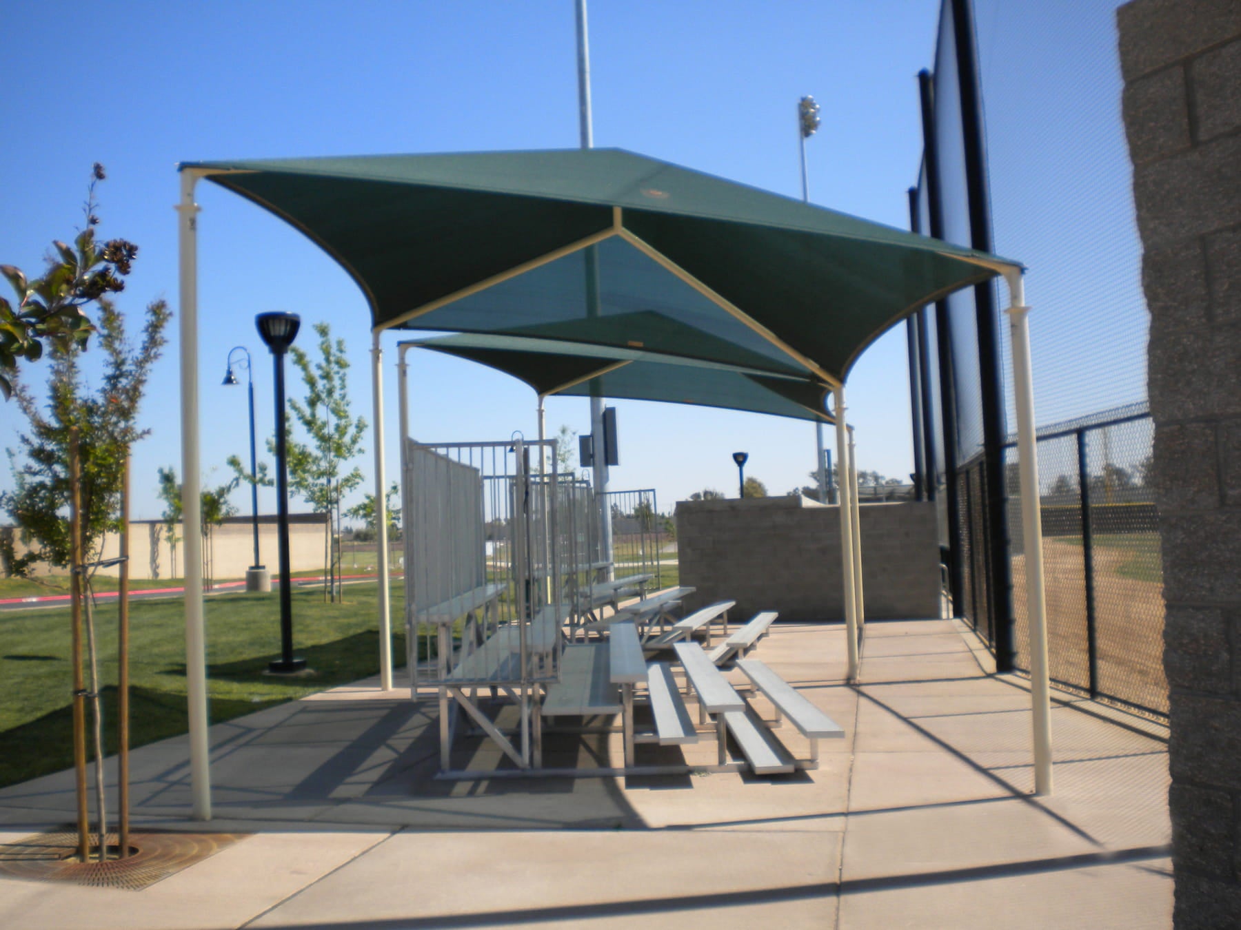 Outdoor seating area with picnic tables and green USA Shade Slant Hip structure in a park setting.