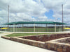 Outdoor sports facility with a green roofed USA Shade Wrap-around Hip and sports field under a cloudy sky.