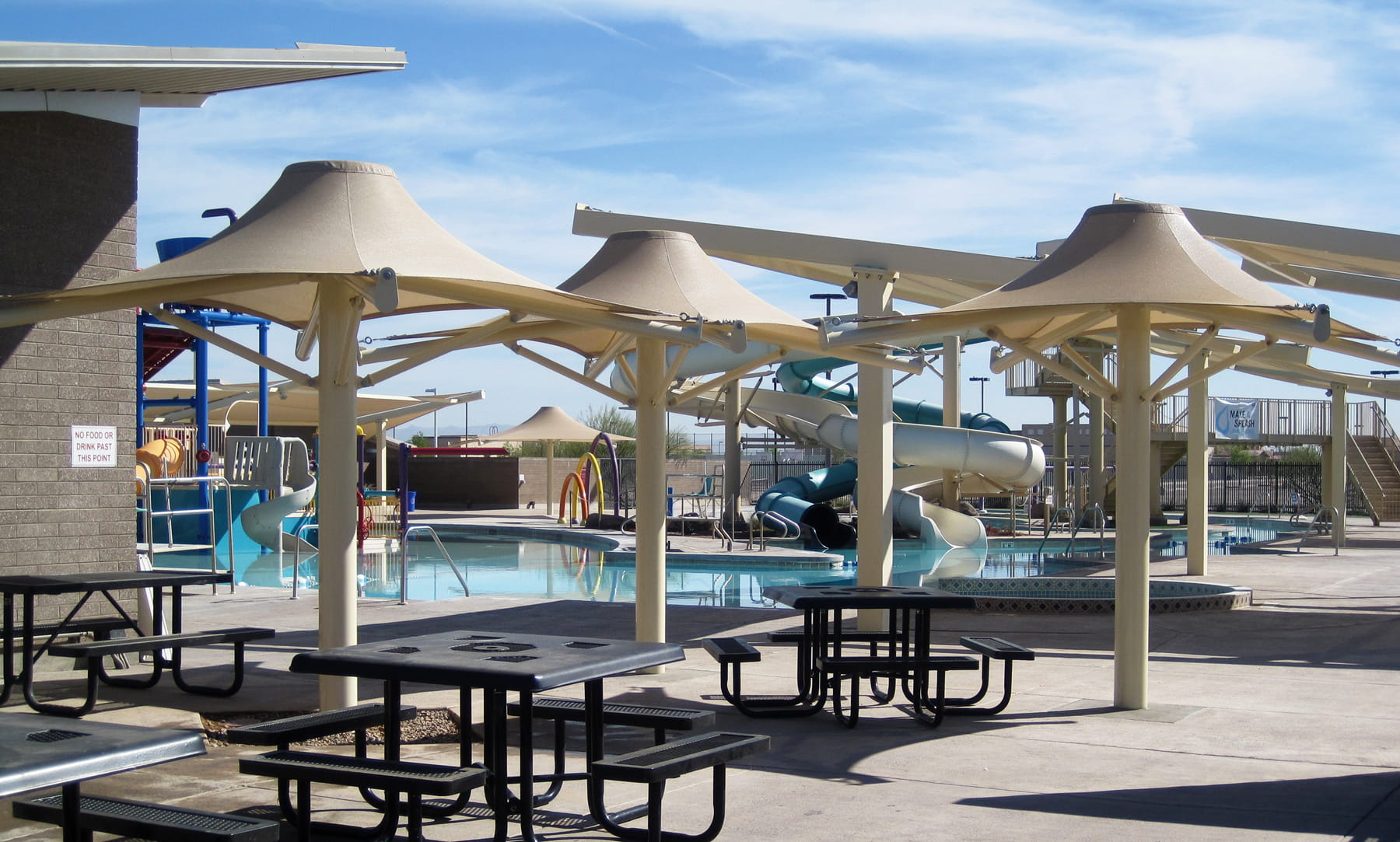 Outdoor pool area with tables, USA Shade 4-point Twilite Umbrellas, and a slide in the background.
