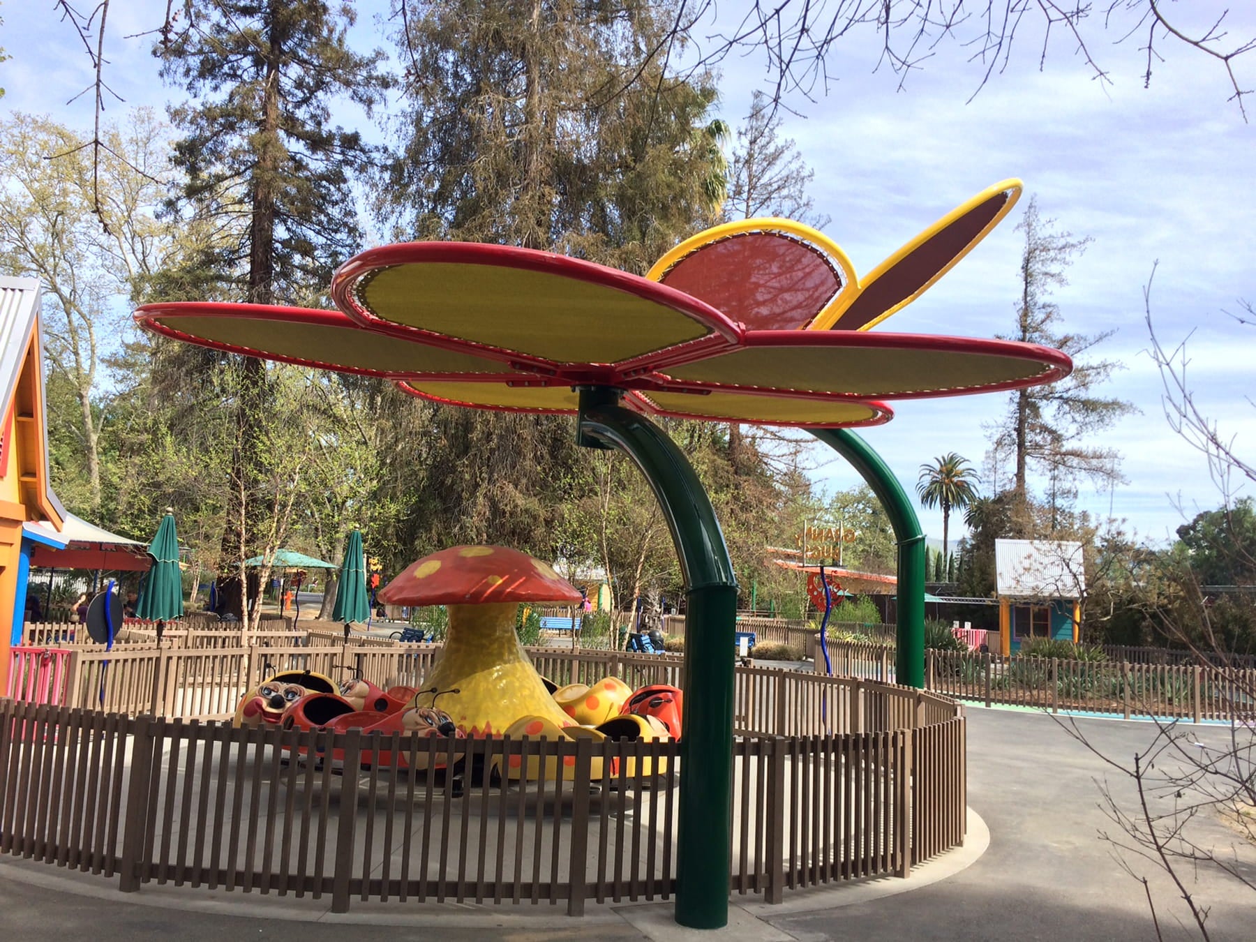 Colorful playground USA Shade Flower Shade Structure shaped like a flower in a park setting with trees and sky.