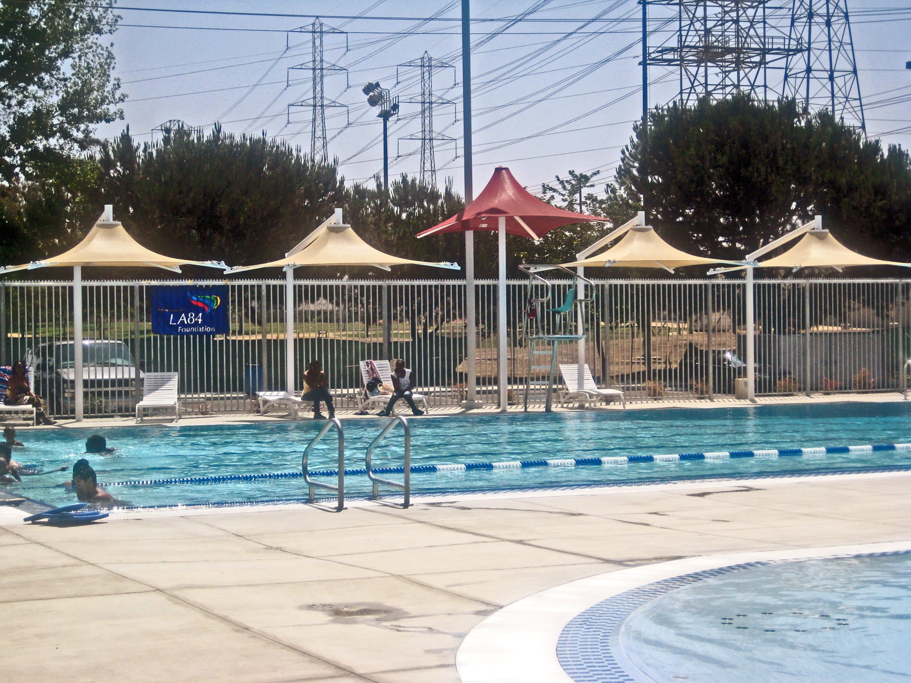 Pool area with lounge chairs, umbrellas including USA Shade Lifeguard Umbrella, and power lines in the background