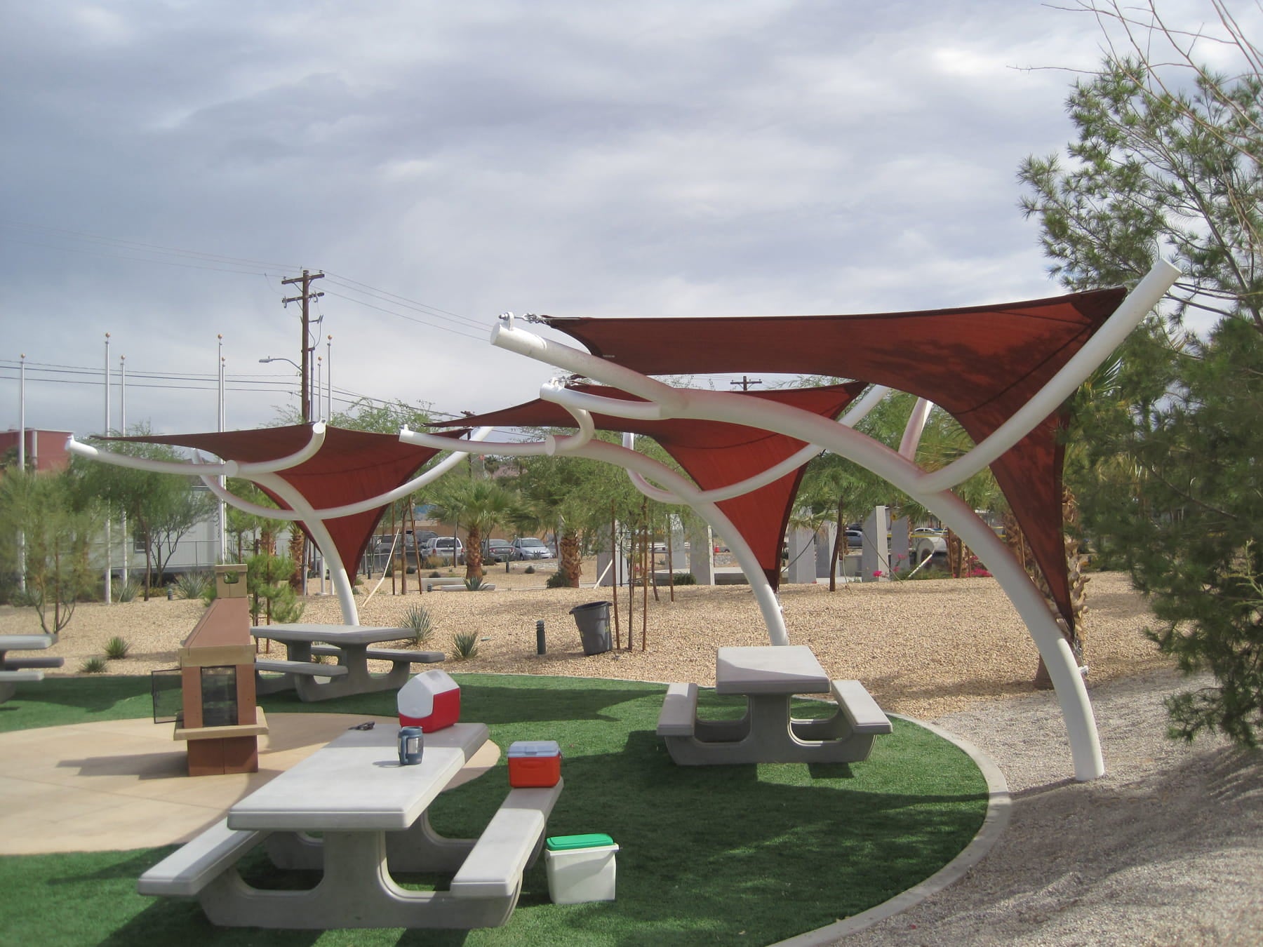 Outdoor picnic area with red USA Shade Pegasus Shade structures and picnic tables in a park setting.