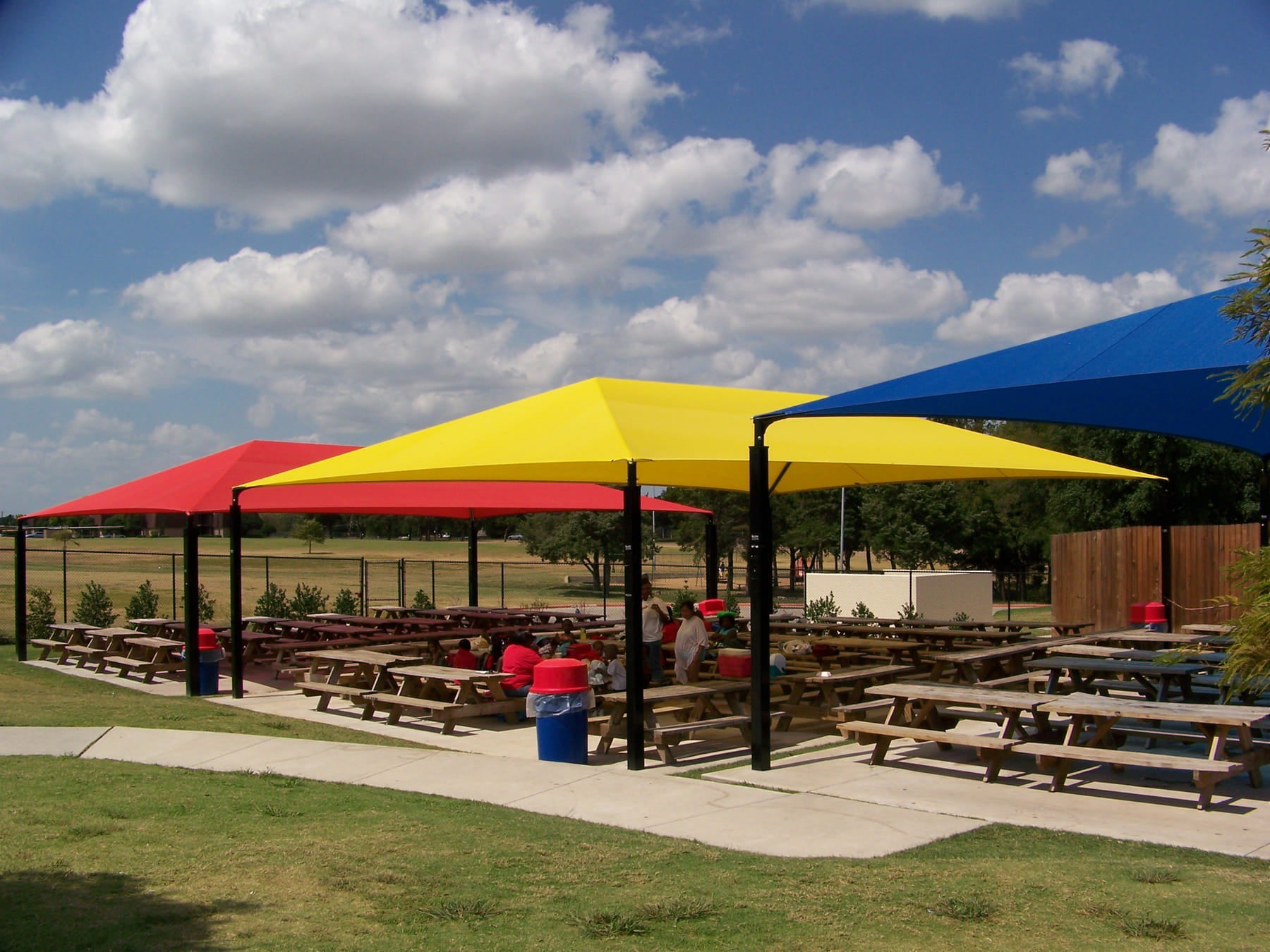 Outdoor seating area with colorful USA Shade Hips and picnic tables under a blue sky.