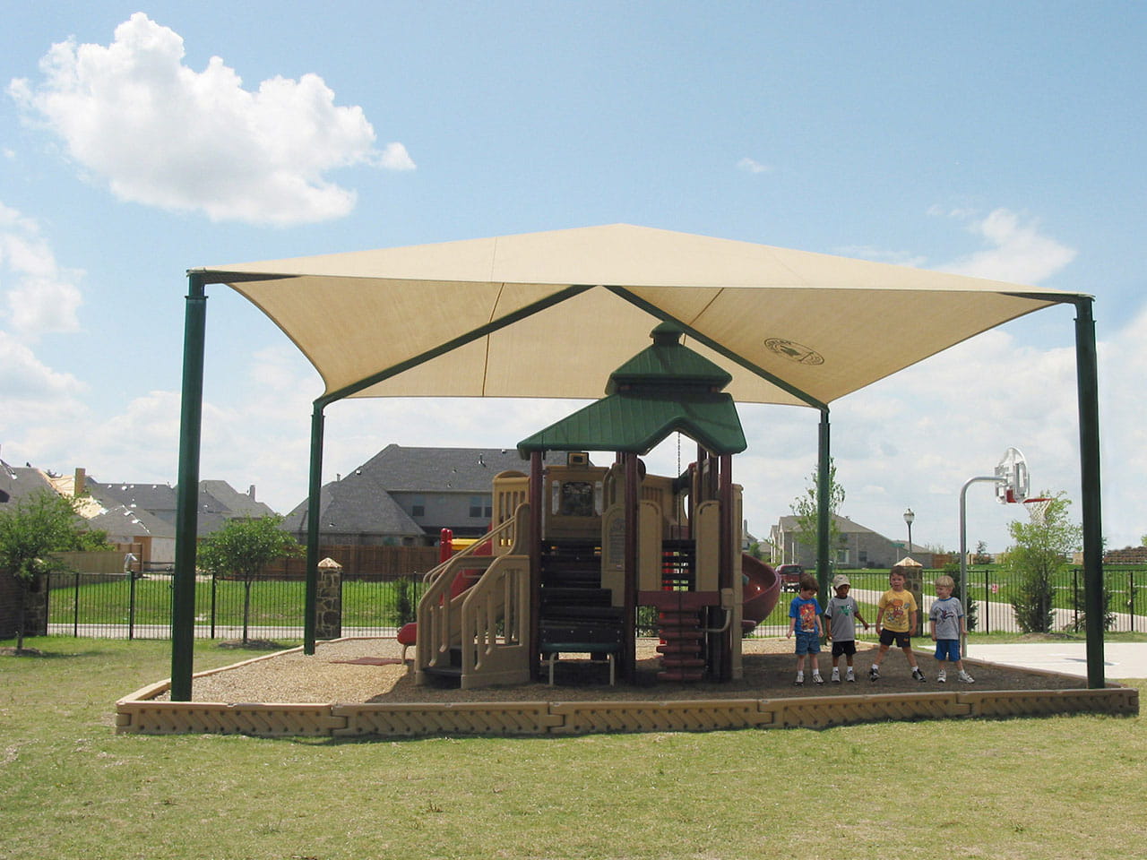 Children's playground with a USA Shade Hip covering on a sunny day with 4 kids standing