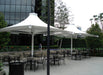 Outdoor seating area with tables, chairs, and large USA Shade 4-point Twilite Umbrellas in a courtyard setting.