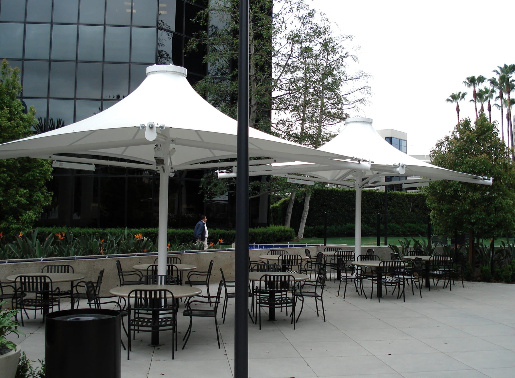 Outdoor seating area with tables, chairs, and large USA Shade 4-point Twilite Umbrellas in a courtyard setting.