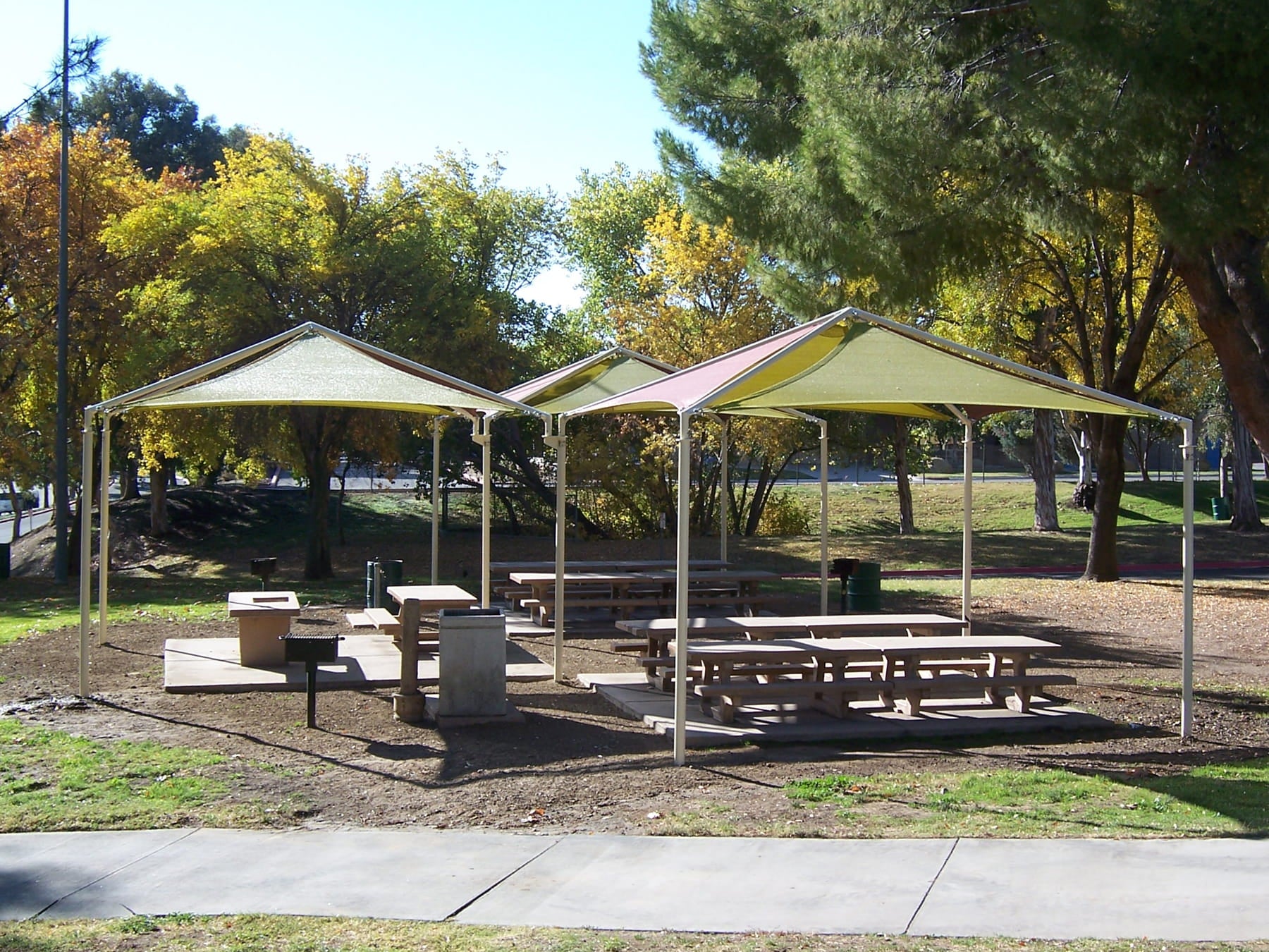 Picnic area with covered USA Shade Multi-Panel Pyramid, tables, and benches in a park setting.