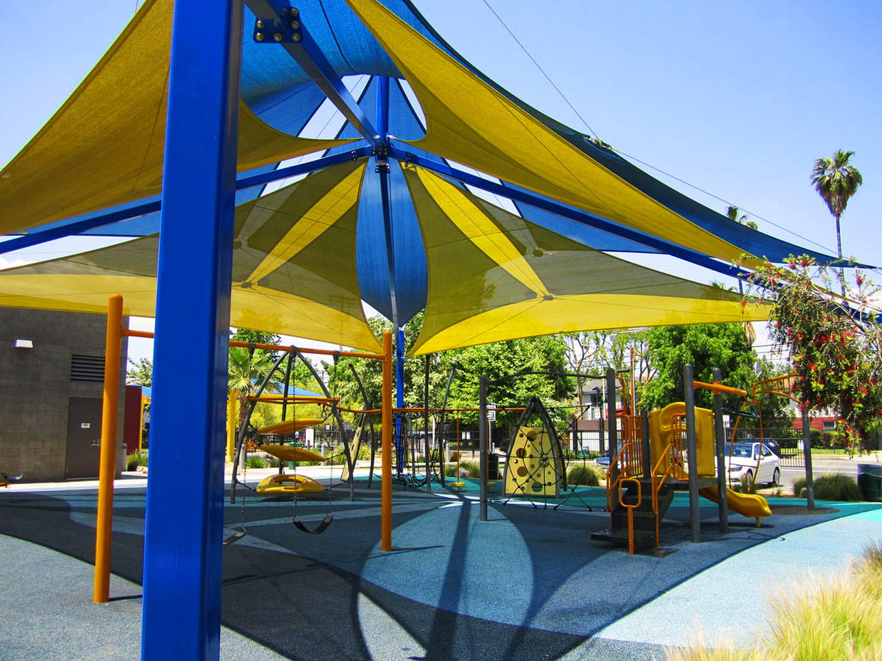 Children's playground with blue and yellow USA Shade Multi-Layer Super Span Pyramid Shades on a sunny day.