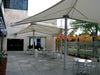 Outdoor patio area with tables and chairs under a large USA Shade Aurora Shade on a sunny day.