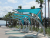 Modern outdoor seating area with turquoise USA Shade Pegasus Shades and white lounge chairs on a beach promenade.