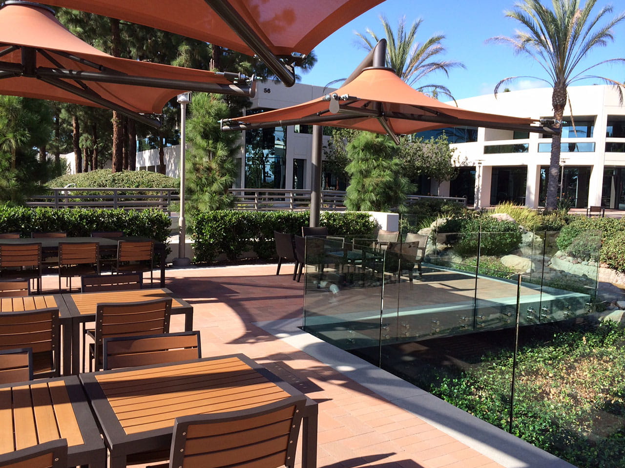 Outdoor seating area with wooden tables and orange USA Shade Solana Cantilevers in a garden setting.