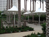 Outdoor seating area with tables, chairs, and USA Shade 4-point Twilite Umbrellas under palm trees and a building.