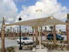 Large outdoor USA Shade 4-point Twilite Umbrella providing shade in a parking lot with palm trees and buildings in the background.