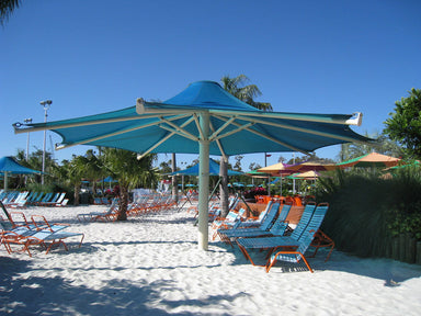 Beach scene with blue USA Shade 8-point Twilite Umbrella and lounge chairs under a clear blue sky.