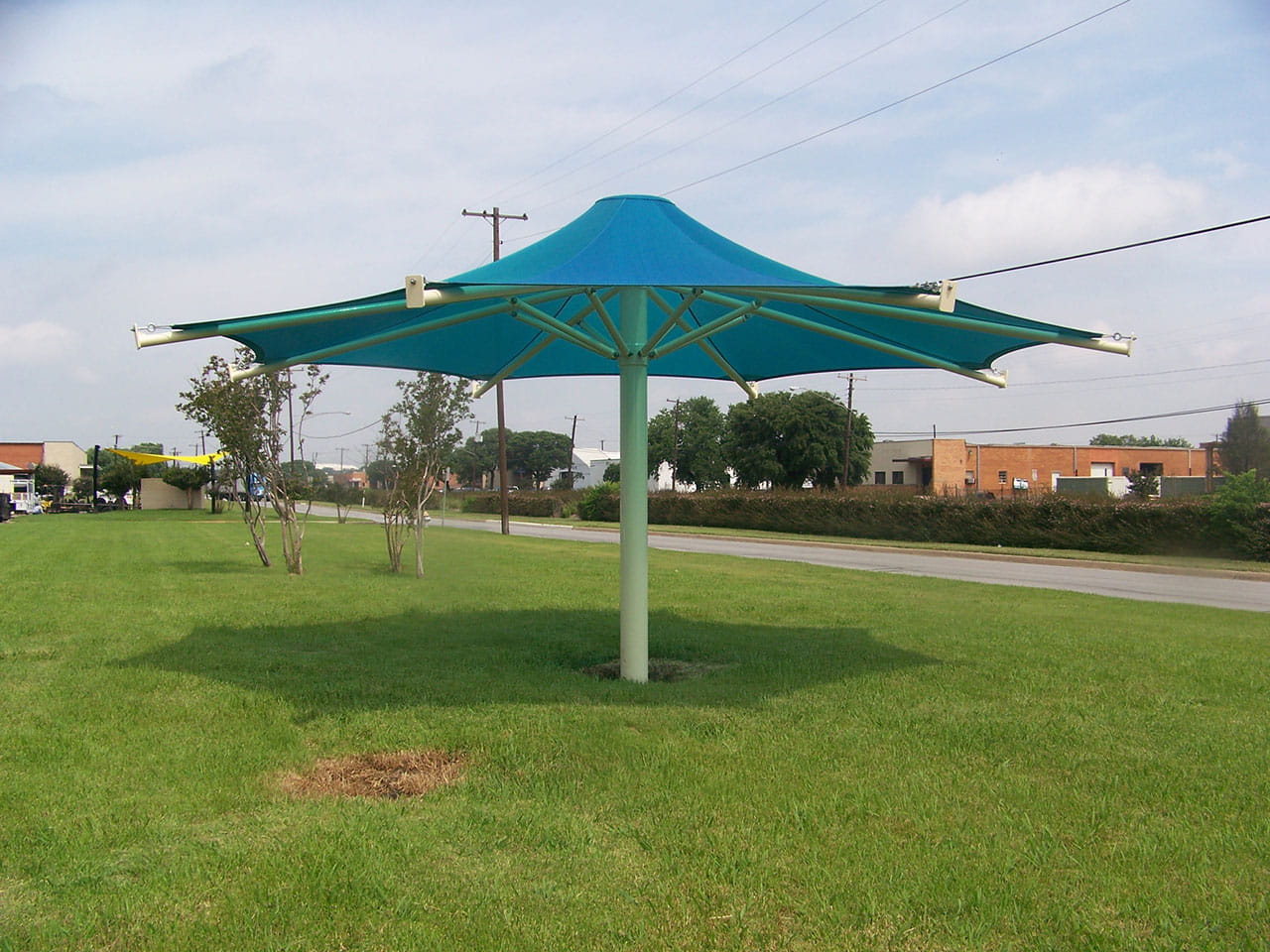 Large blue USA Shade 8-point Twilite Umbrella on a grassy area with buildings and trees in the background