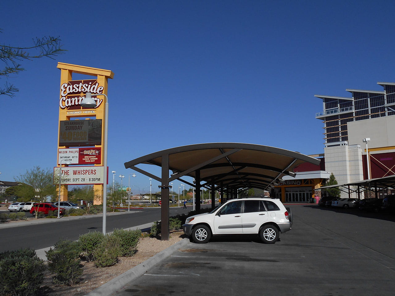 White SUV parked under a USA Shade Panorama Cantilever covered area with a 'Eastside' sign in the background.
