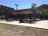 Outdoor seating area with tables and benches in front of a building with USA Shade Panorama Cantilever providing shade