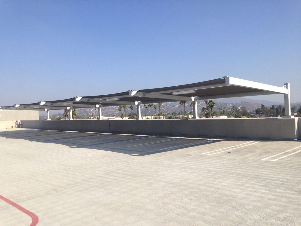 Parking lot with a USA Shade Slanted Cantilever Cabled covered area under a clear blue sky