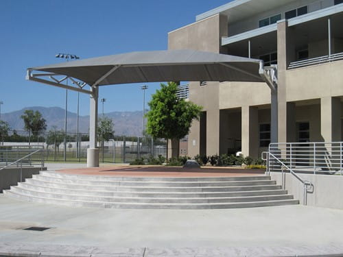 Outdoor seating area with a large USA Shade Tri-Truss Cantilever and steps leading up to a building.