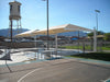 Outdoor sports facility with a large white USA Shade Full Hip Cantilever Shade, basketball court, and water tower in the background.