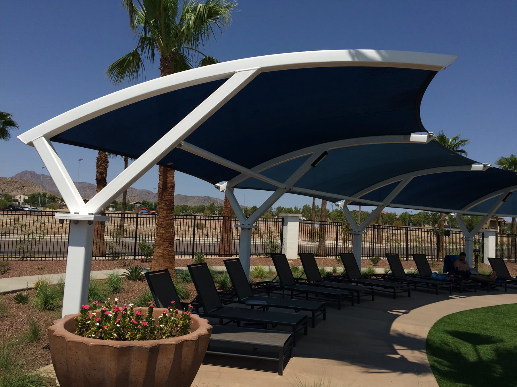 Outdoor seating area with blue USA Shade Panorama Cantilever and lounge chairs under a clear blue sky.