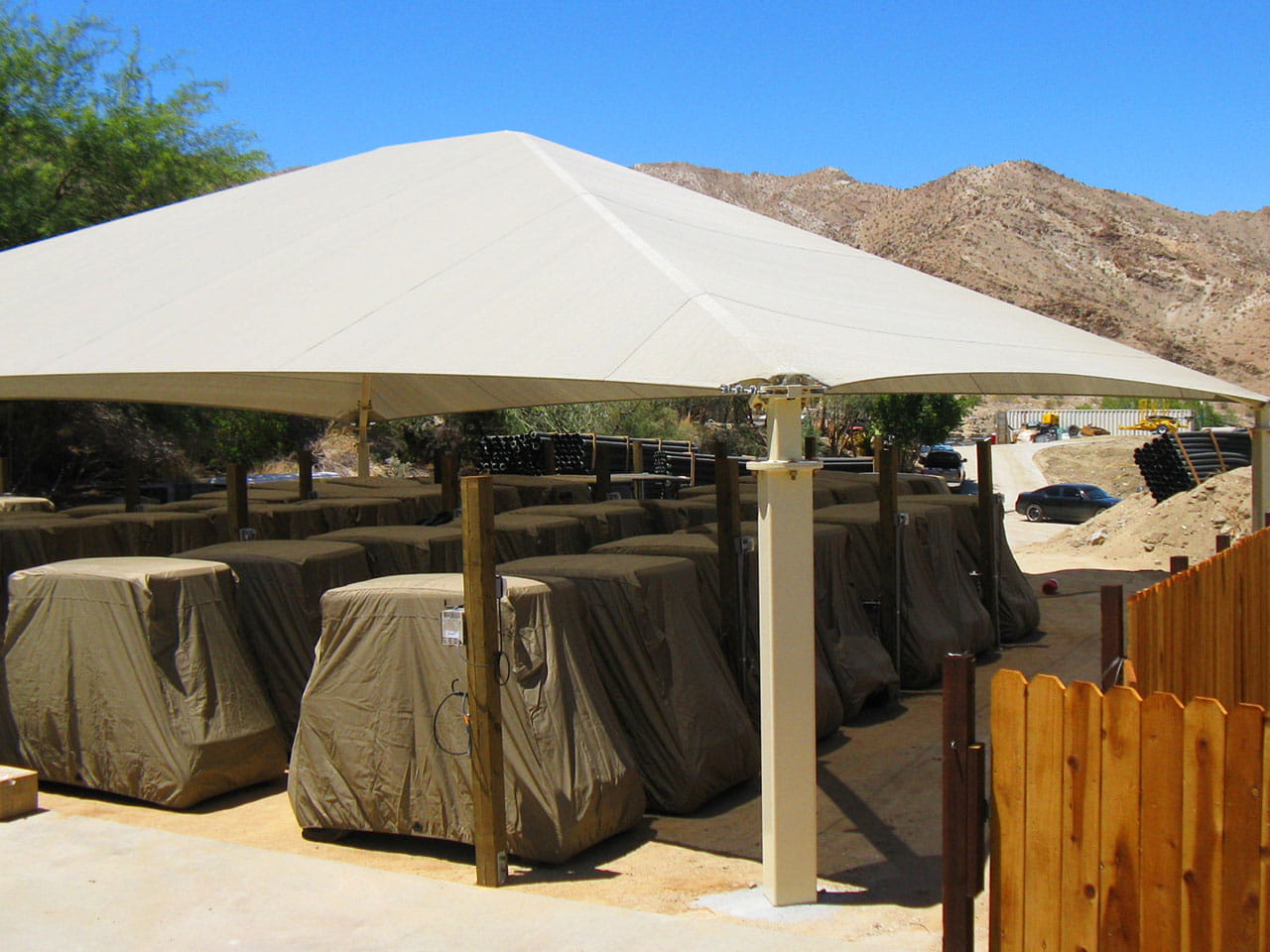 Beige outdoor USA Shade Super Span Hip with covered furniture underneath, set against a mountainous landscape.