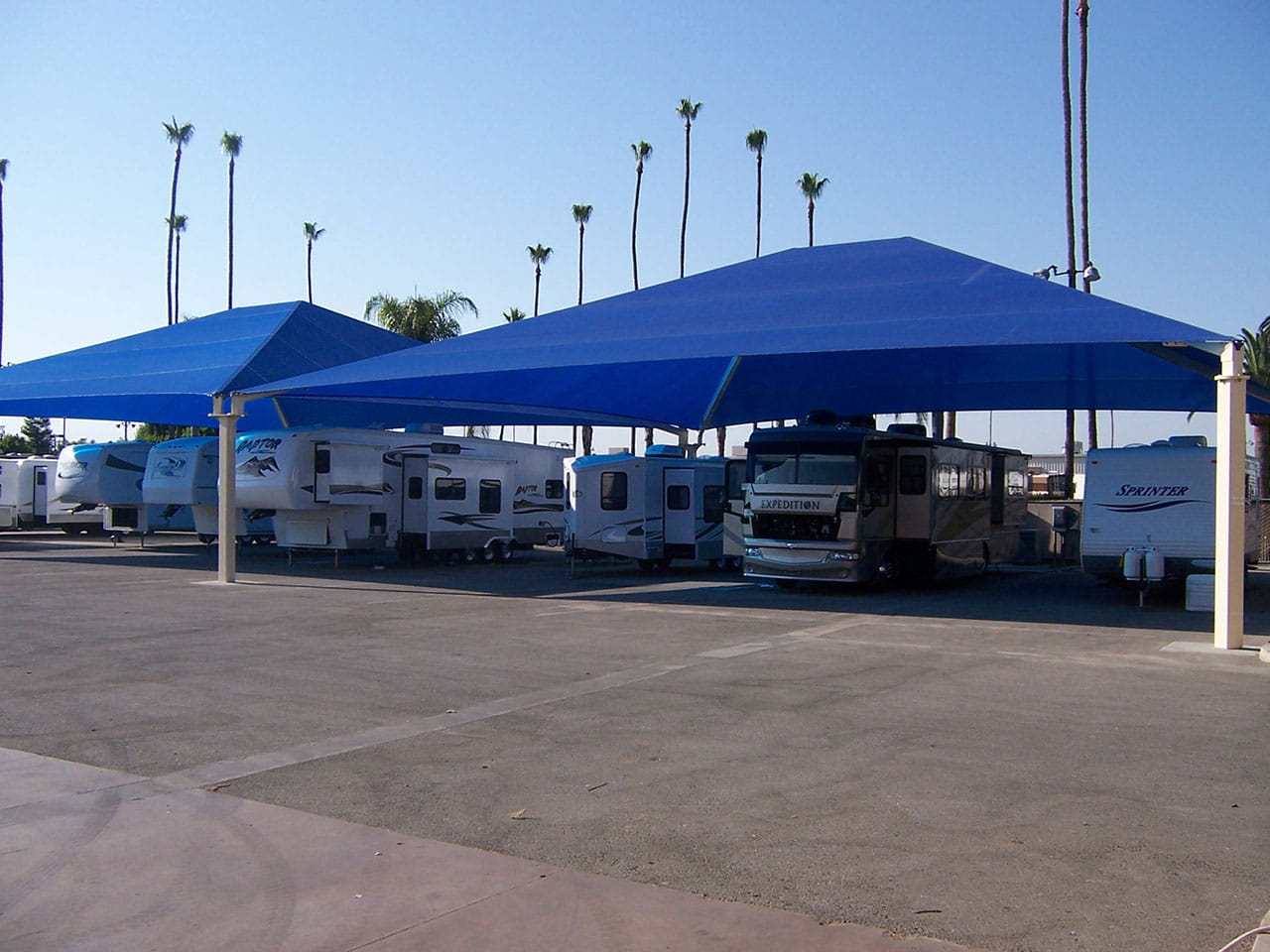 RVs under blue USA Shade Super Span Hip with palm trees in the background