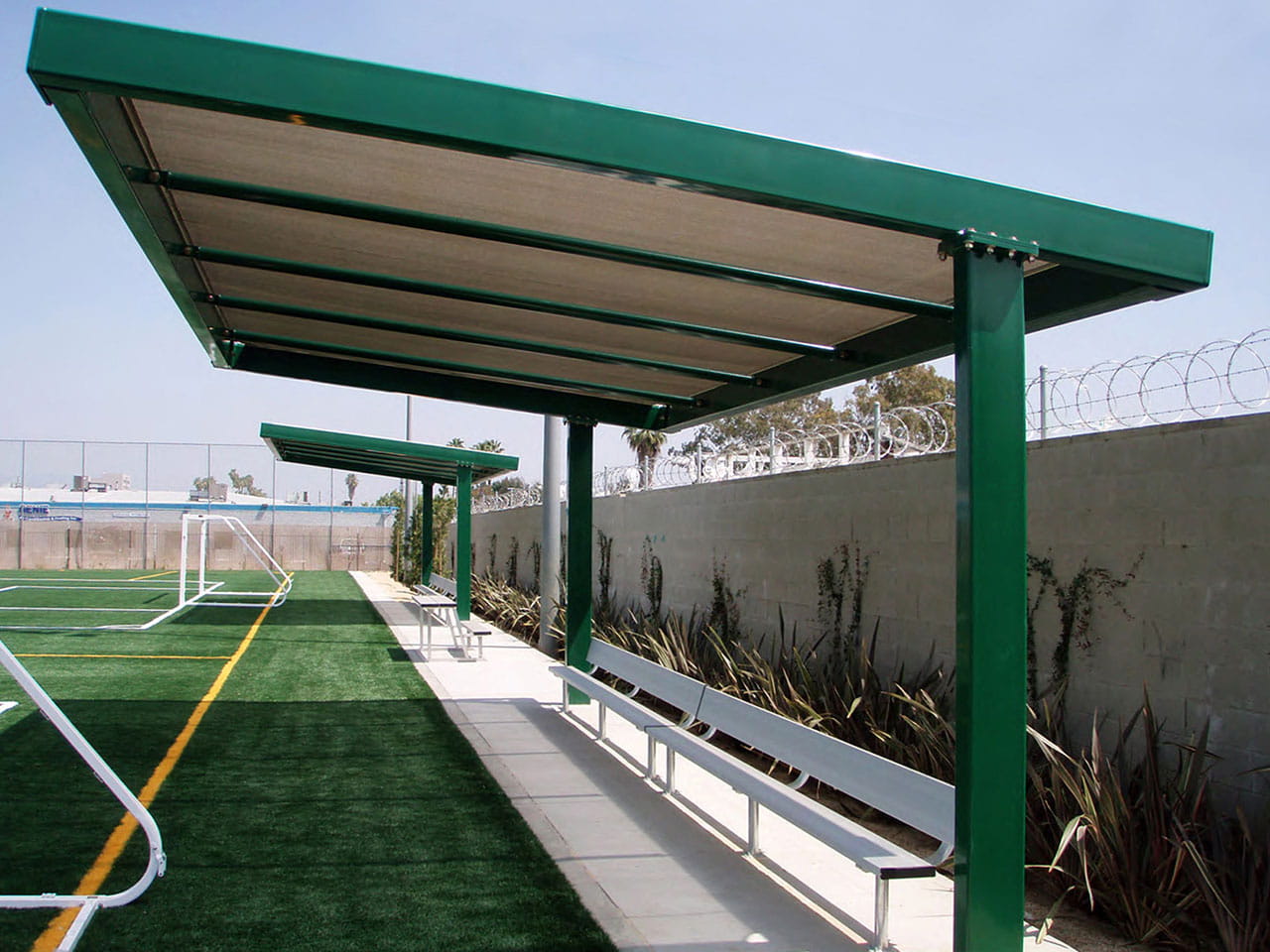 Green metal USA Shade Slanted Cantilever Framed over a sports field with artificial grass and a clear sky.