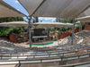 Outdoor amphitheater with tiered seating and stage setup under large USA Shade Hips.