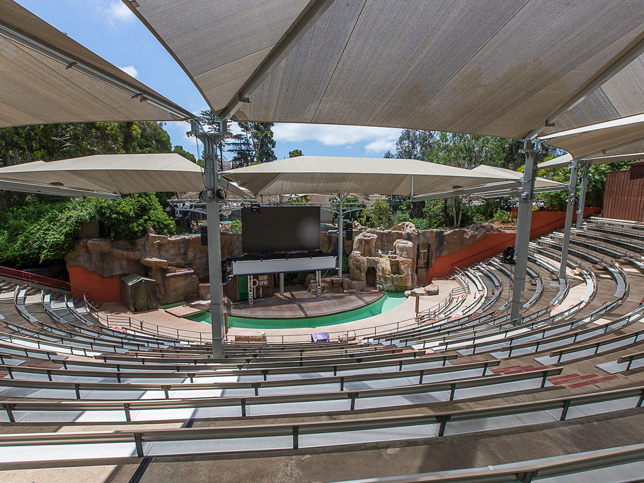 Outdoor amphitheater with tiered seating and stage setup under large USA Shade Hips.