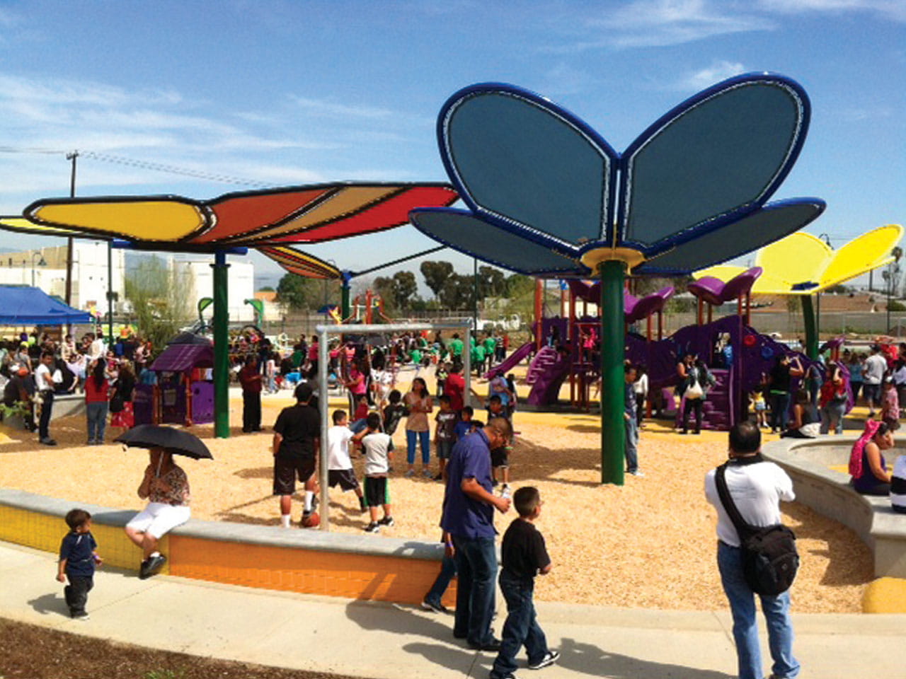 Colorful playground with USA Shade Flower Shade Structure and children playing on a sunny day.
