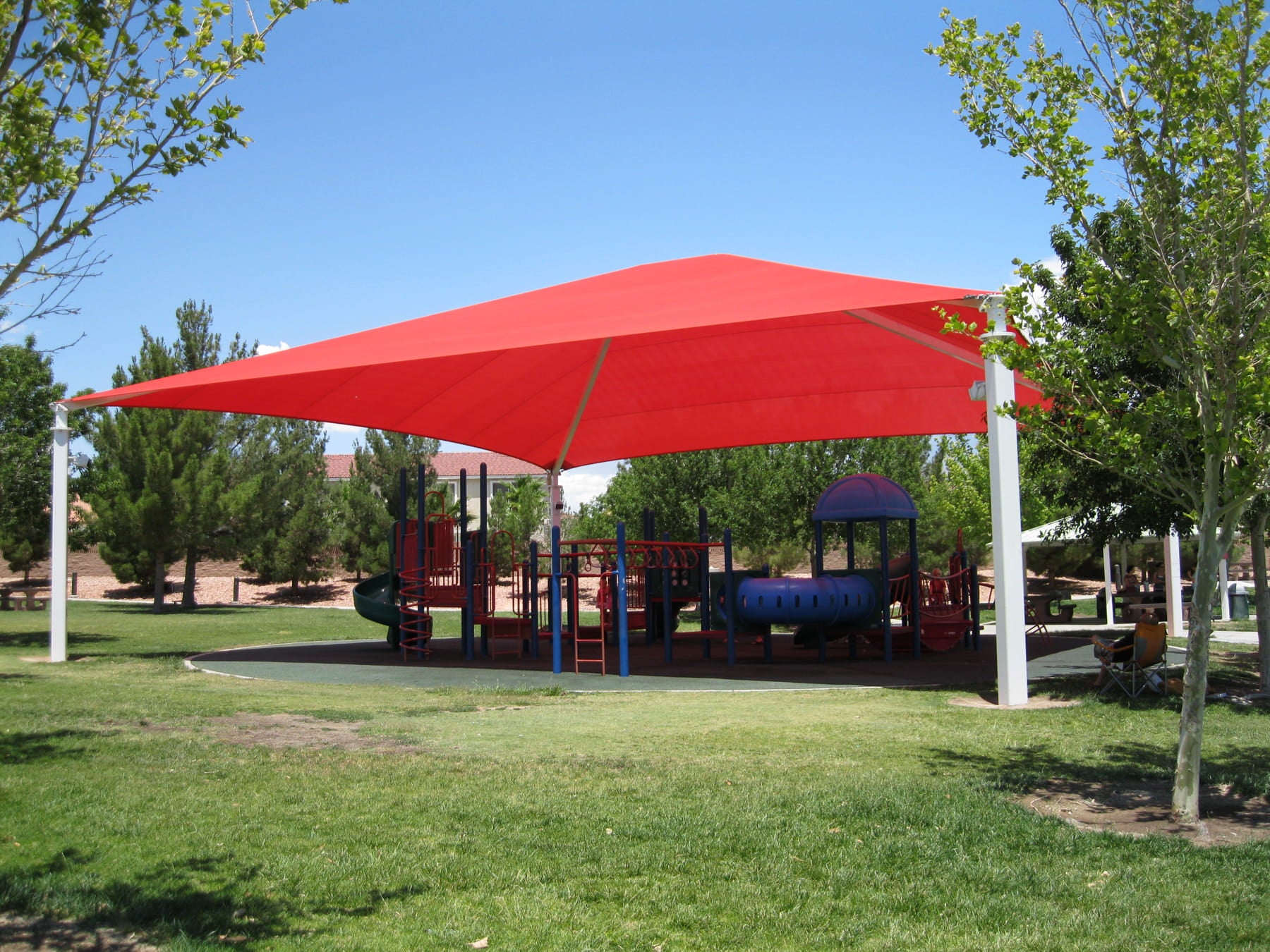 Red USA Shade Hip over a playground area with trees and clear sky in the background
