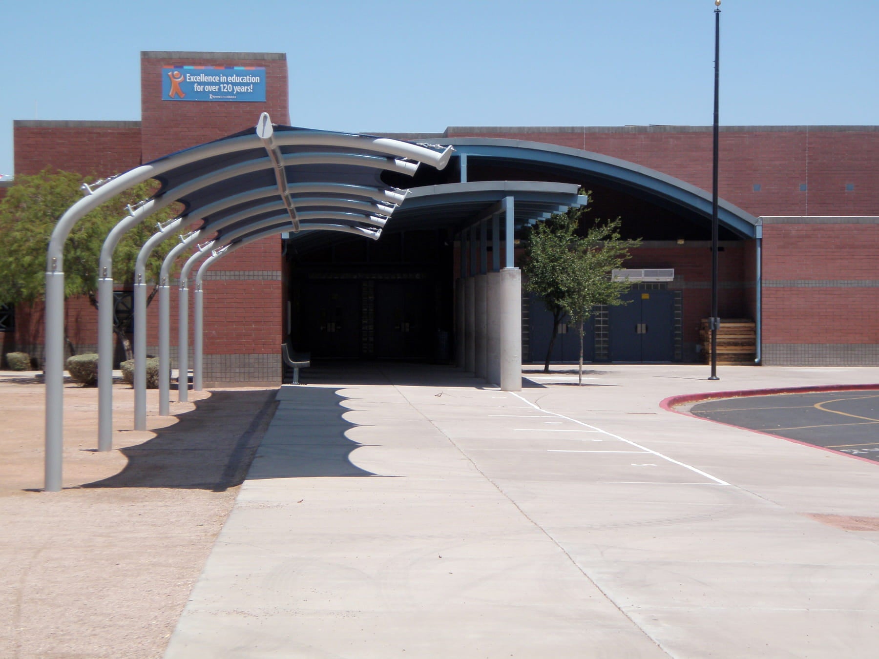 USA Shade Cantilever Arch Walkway Covered walkway leading to a building with a blue sign on a clear day.