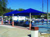 Outdoor seating area with blue USA Shade Pyramid Shades and benches under a clear blue sky.