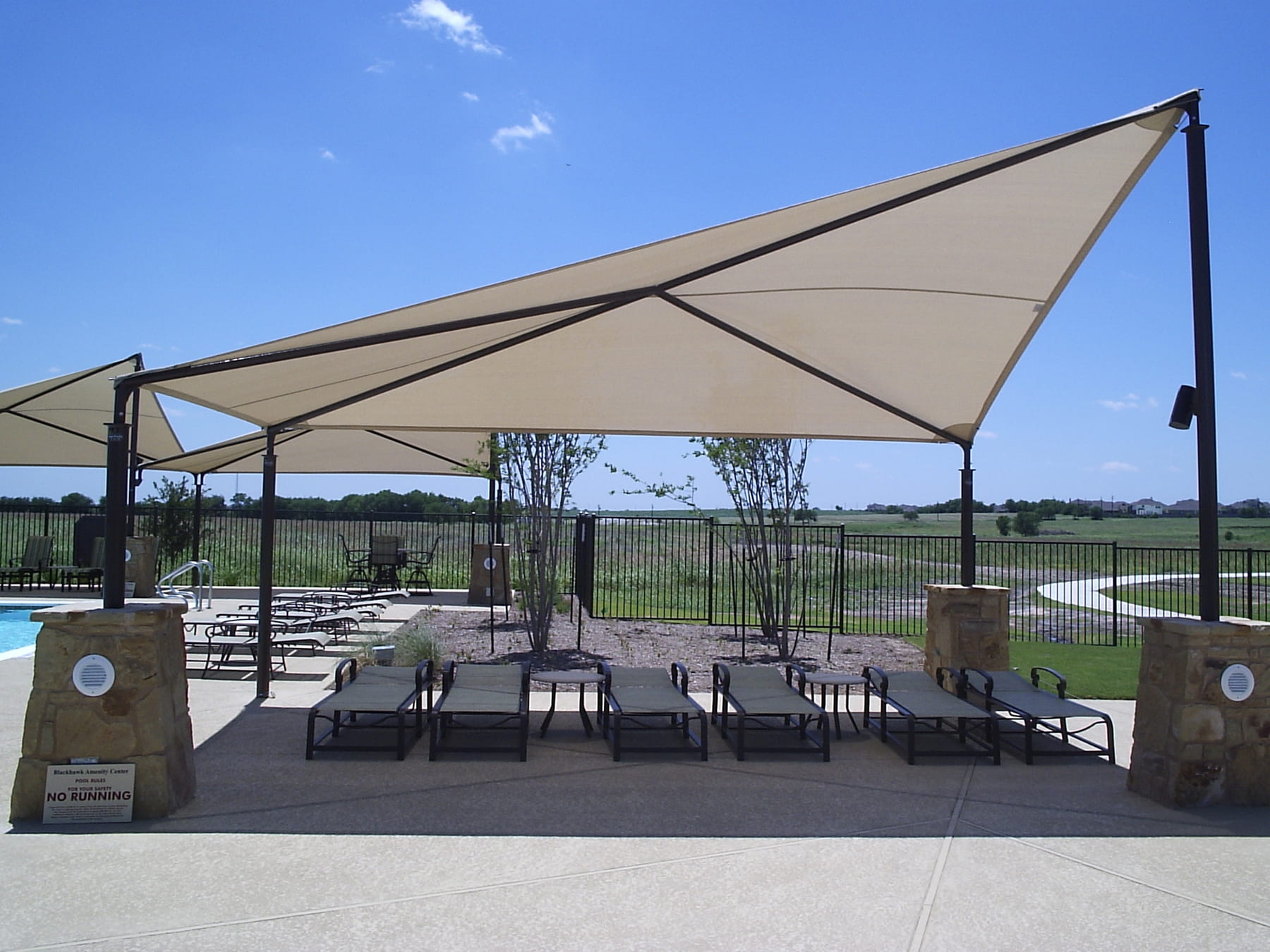 Beige USA Shade Wave Shade over outdoor seating area with tables and chairs on a clear day.